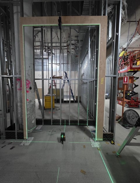 Construction site with metal framed door opening and drywall frame, ladder inside, tools visible on floor, industrial workshop setting
